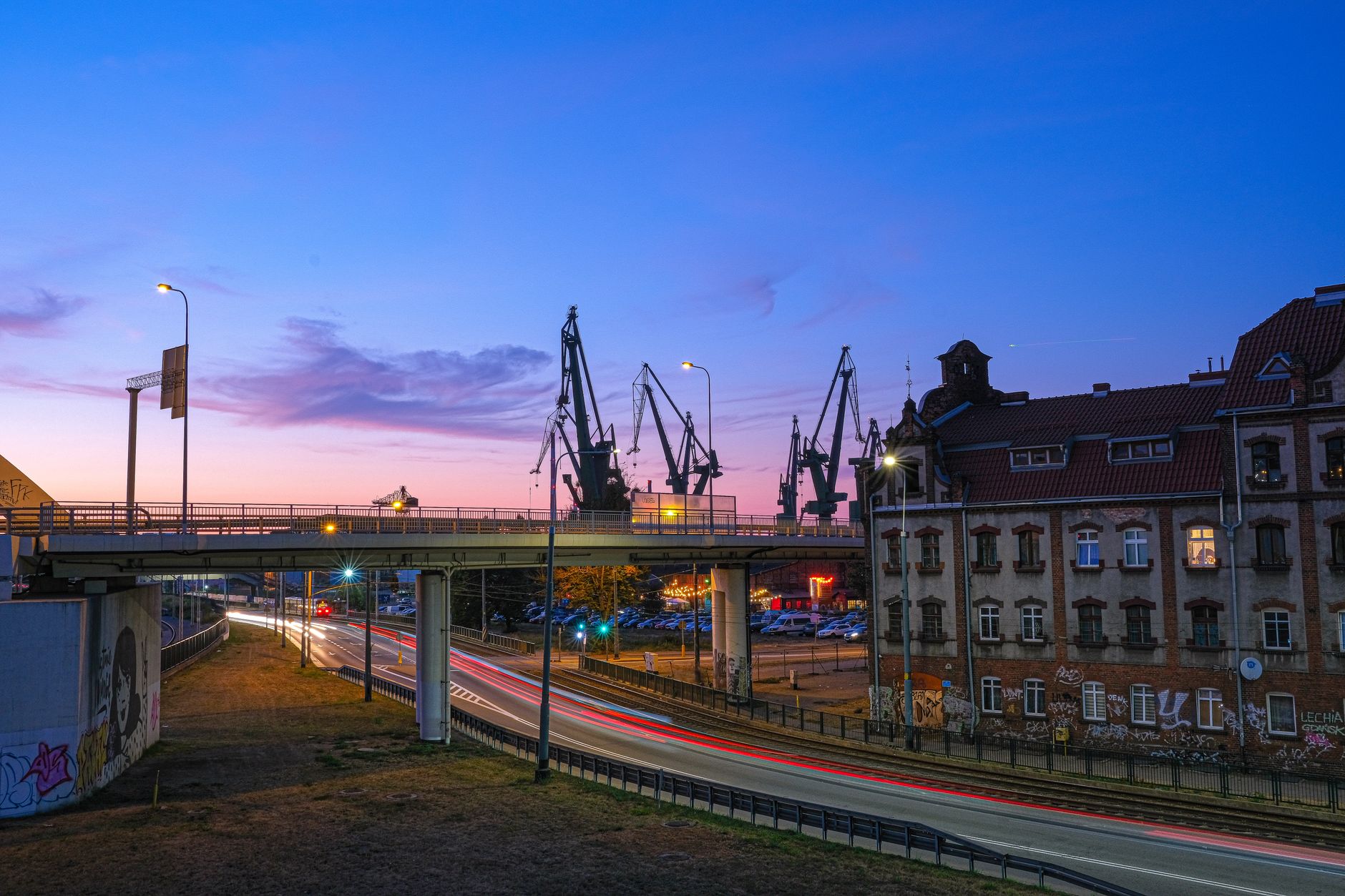 Evening view of a bridge and industrial cranes in Gdańsk, Poland, under a colorful sunset sky. — Trójmiasto