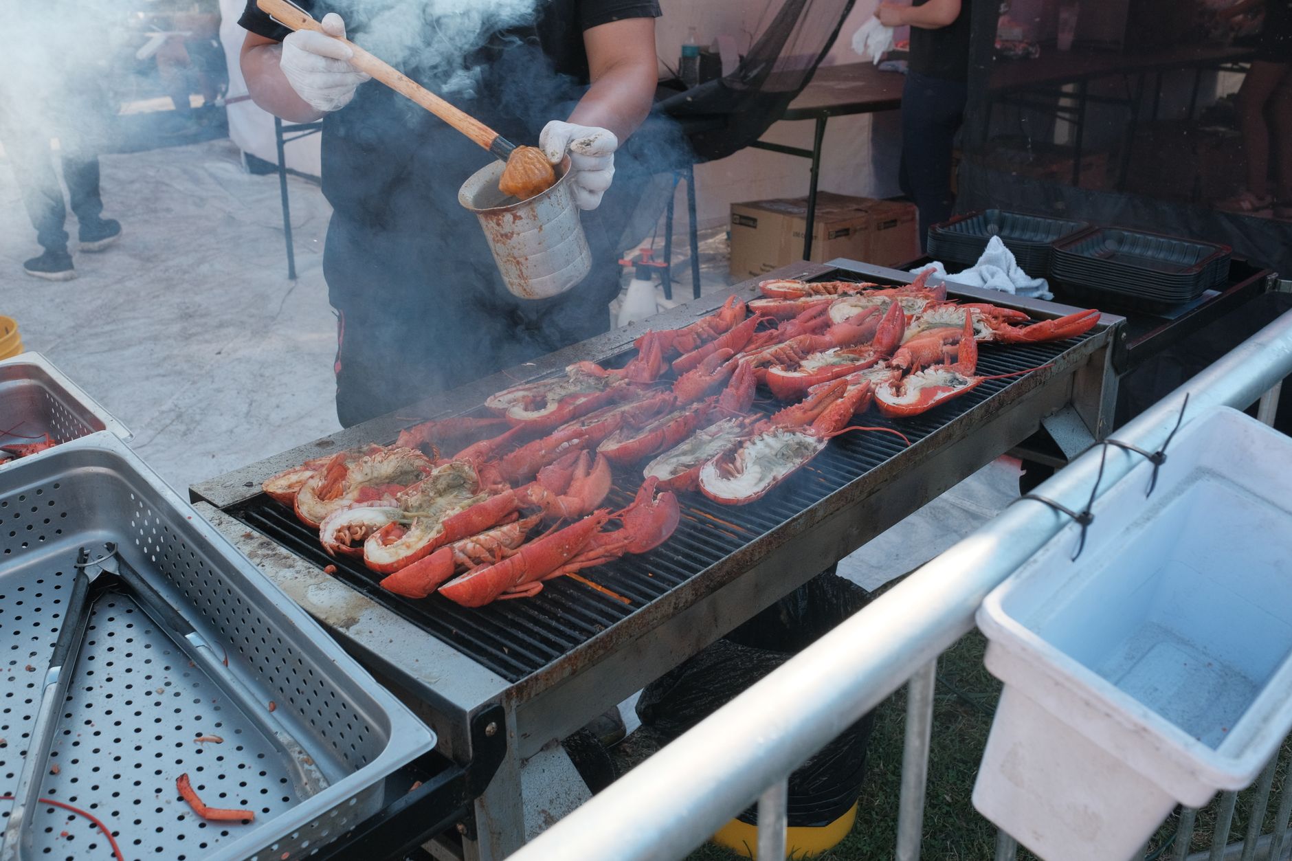 Lobsters being grilled by a man at an outdoor barbecue event with smoke rising. — Trójmiasto