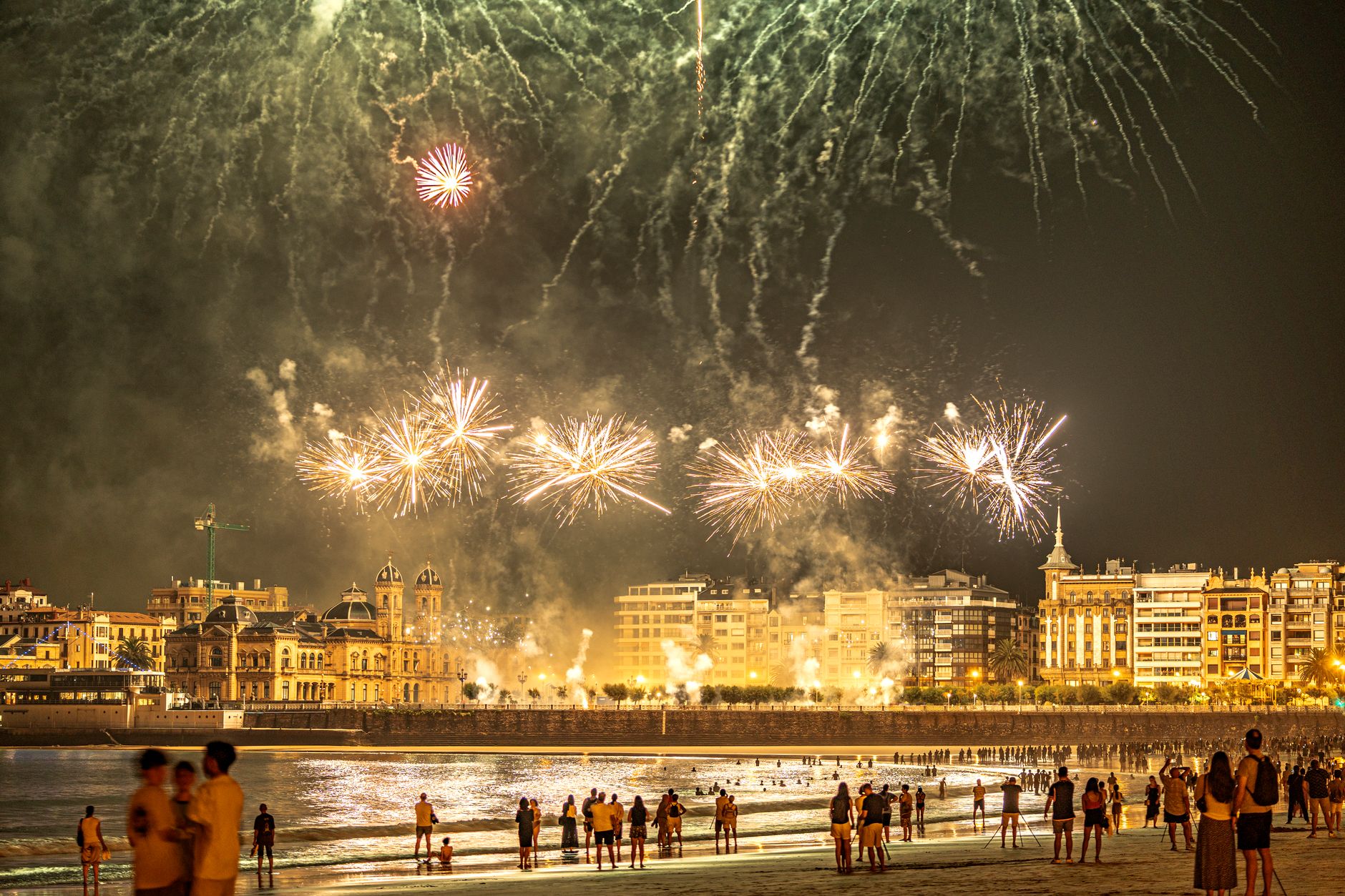 Vibrant fireworks light up the night sky over a bustling city beach. — Trójmiasto