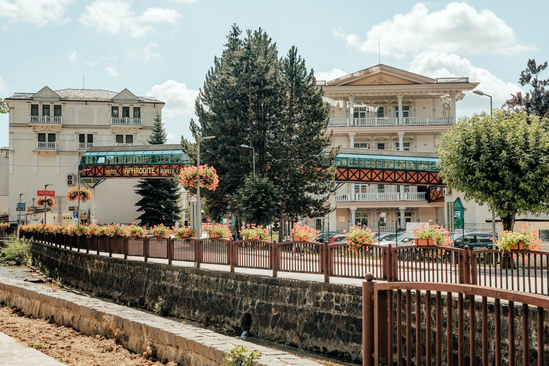 Exterior view of Hotel Aphrodite surrounded by lush greenery and floral displays under a bright blue sky. — Trójmiasto