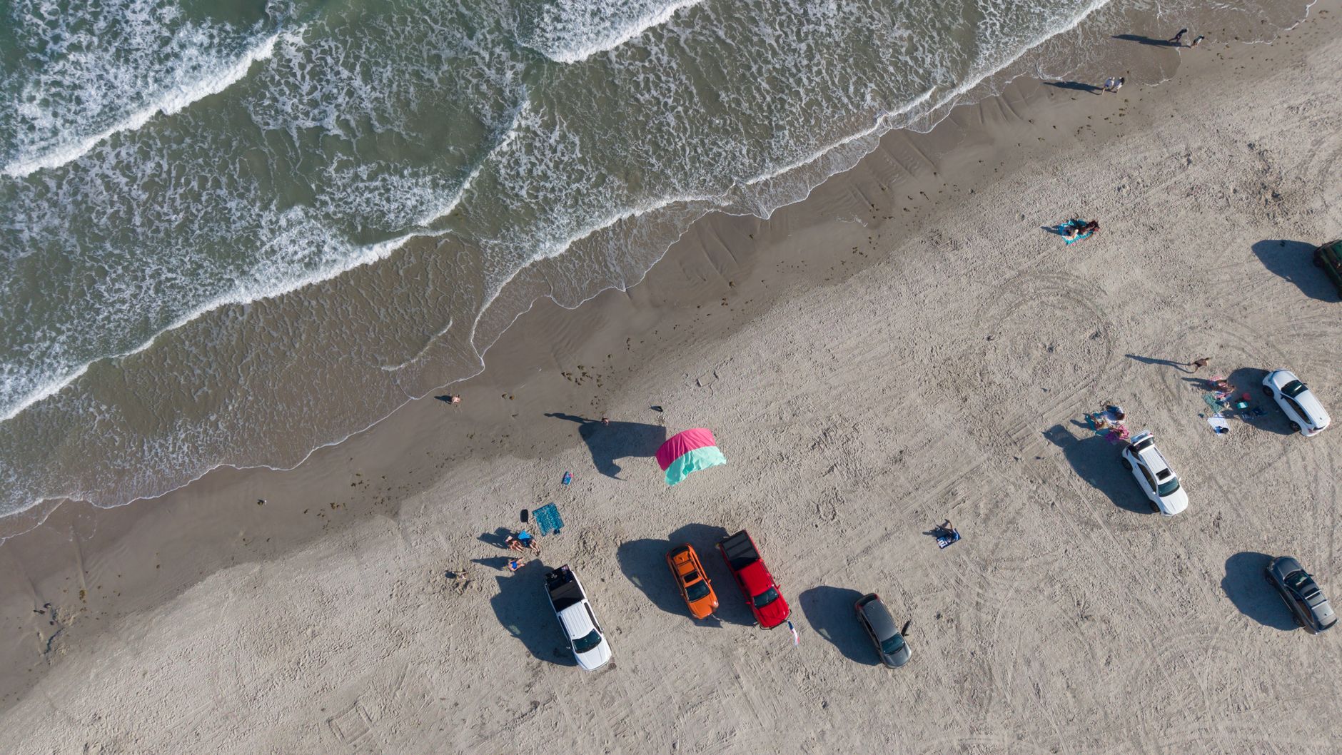 Top-down aerial shot of a sunny day at the beach in Corpus Christi, Texas with cars parked along the shoreline. — Trójmiasto