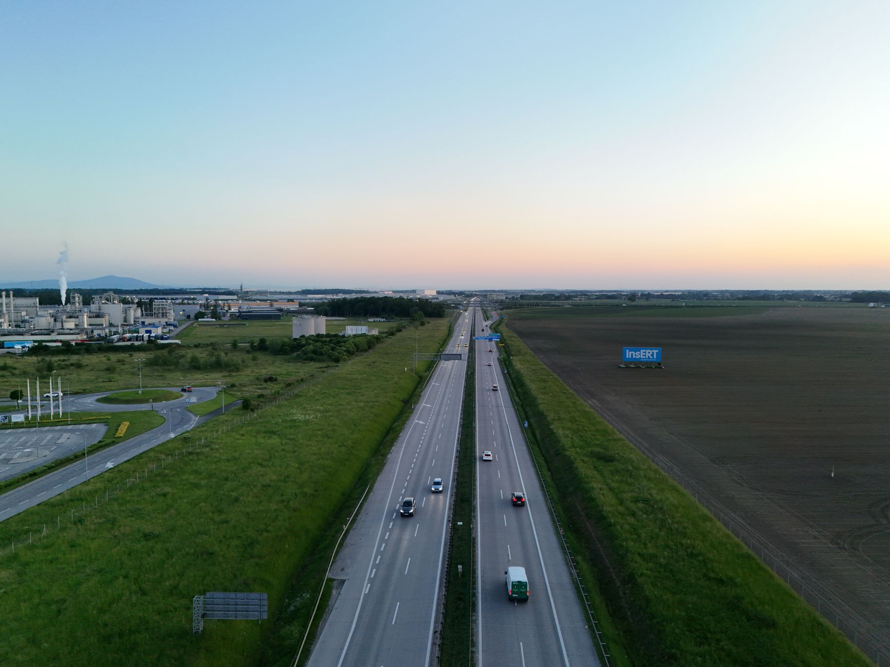 Aerial photograph shows a highway at sunset near a factory and fields. — Trójmiasto