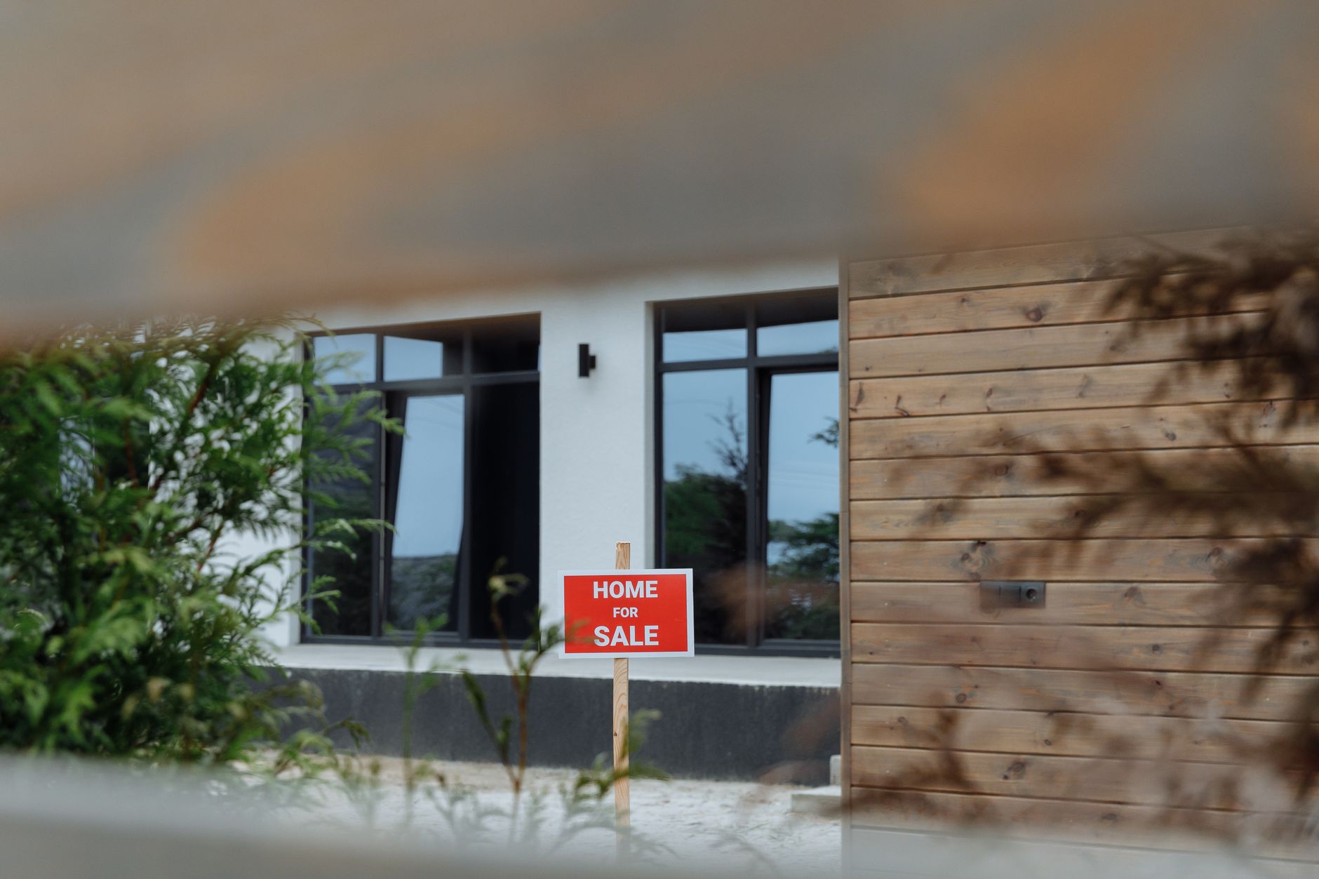 A contemporary home with a 'For Sale' sign in the front yard, framed by greenery. — Trójmiasto