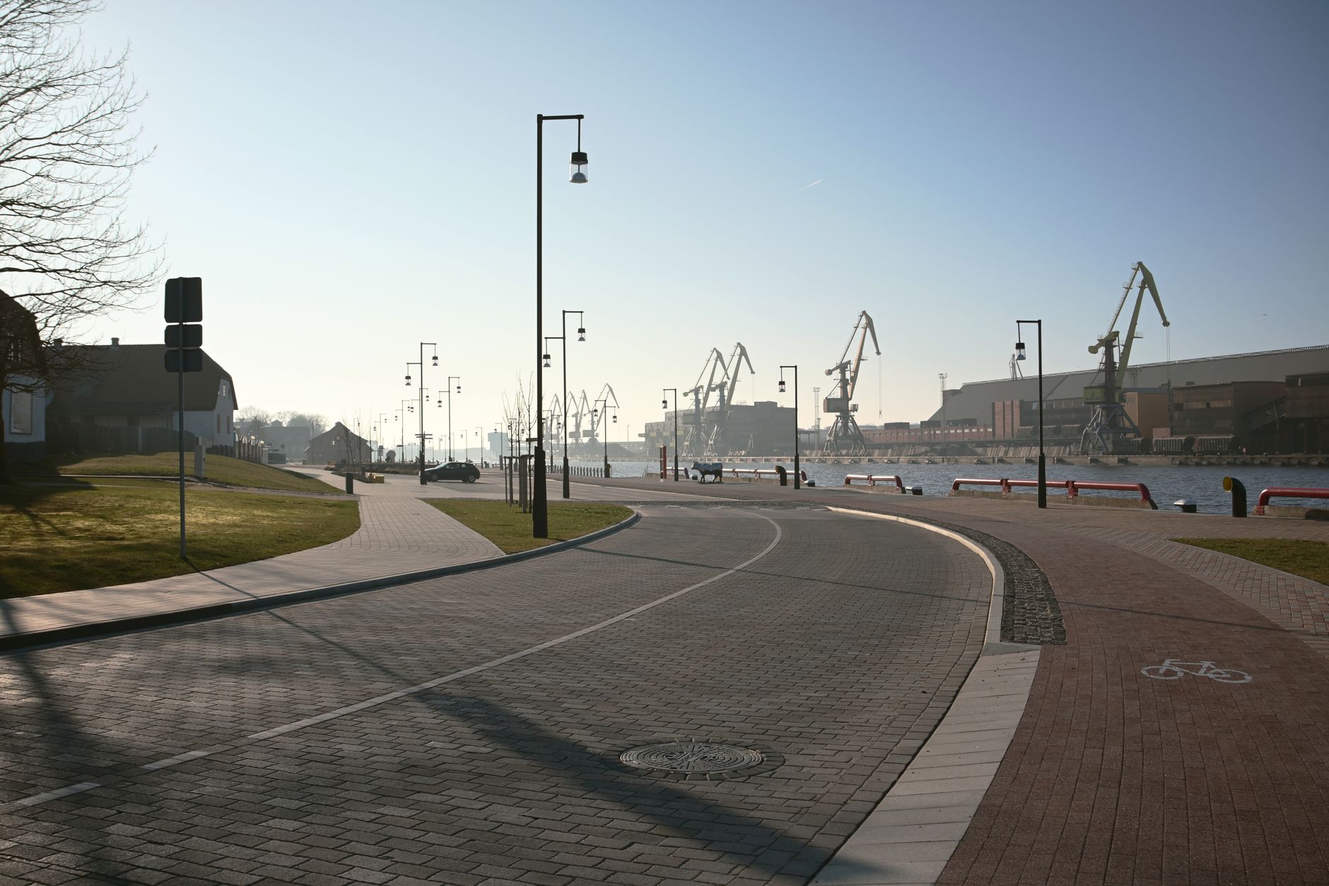 A serene view of the Ventspils promenade and harbor with prominent cranes under a clear sky. — Trójmiasto