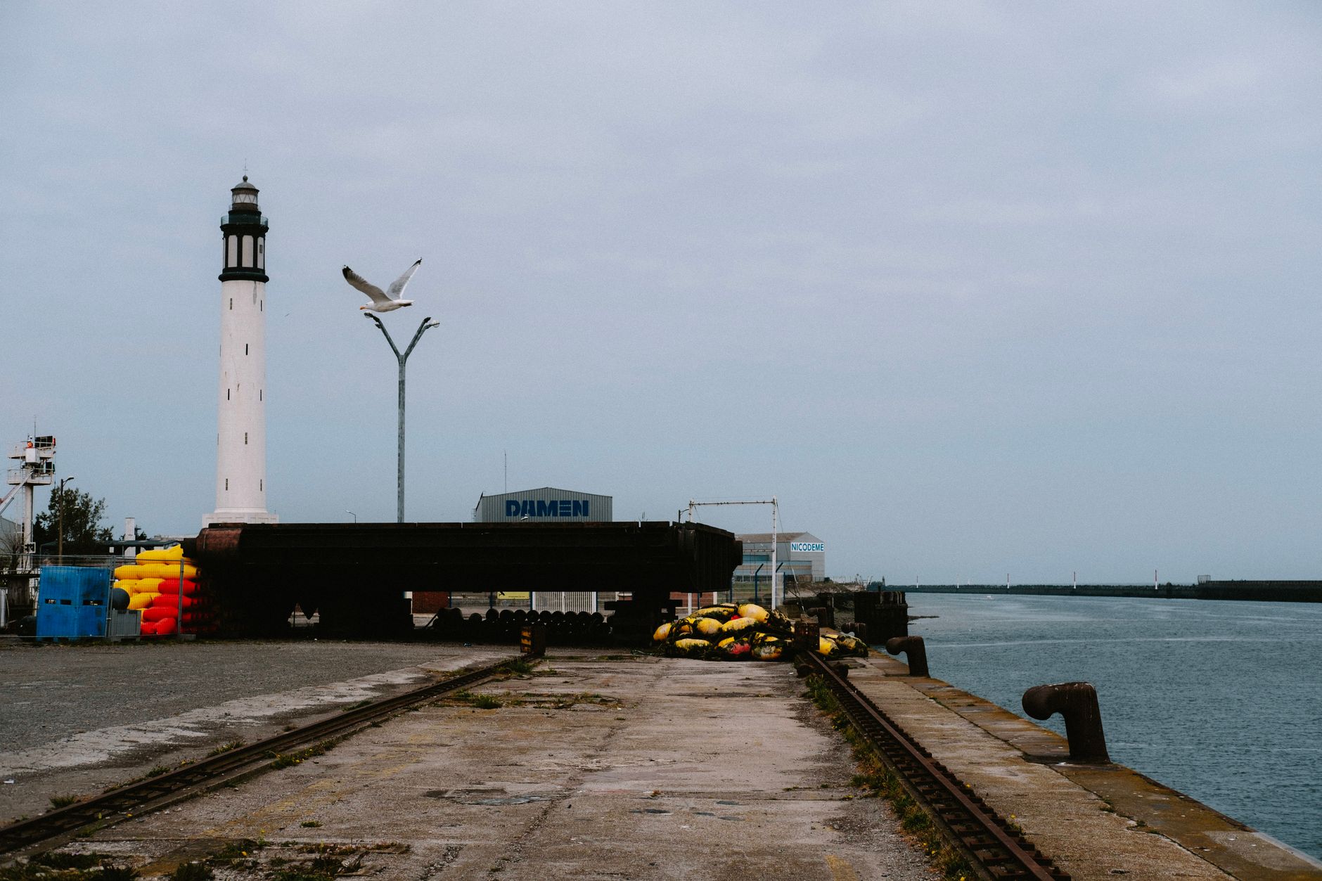 A serene view of a lighthouse by the harbor with a seagull in flight, industrial setting. — Trójmiasto