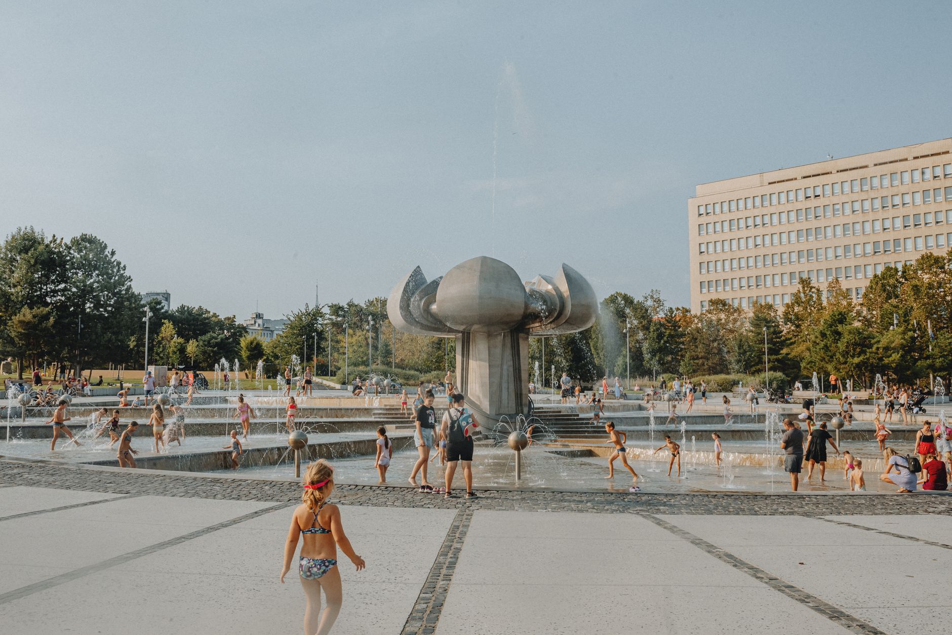 Children enjoying a sunny day at an urban park fountain with modern architecture. — Trójmiasto