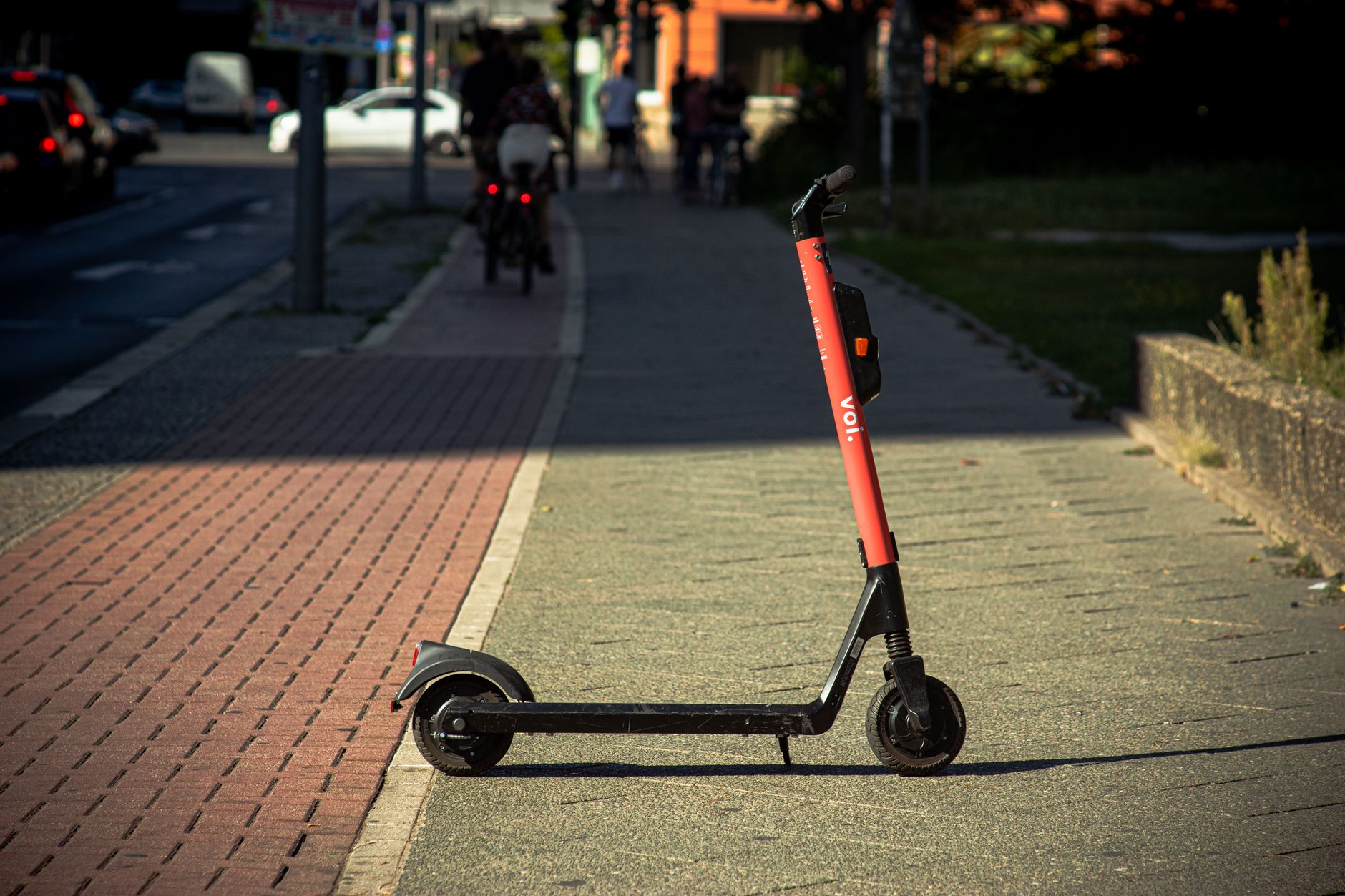 A Voi e-scooter parked on a sunlit city sidewalk with a blurred urban background. — Trójmiasto