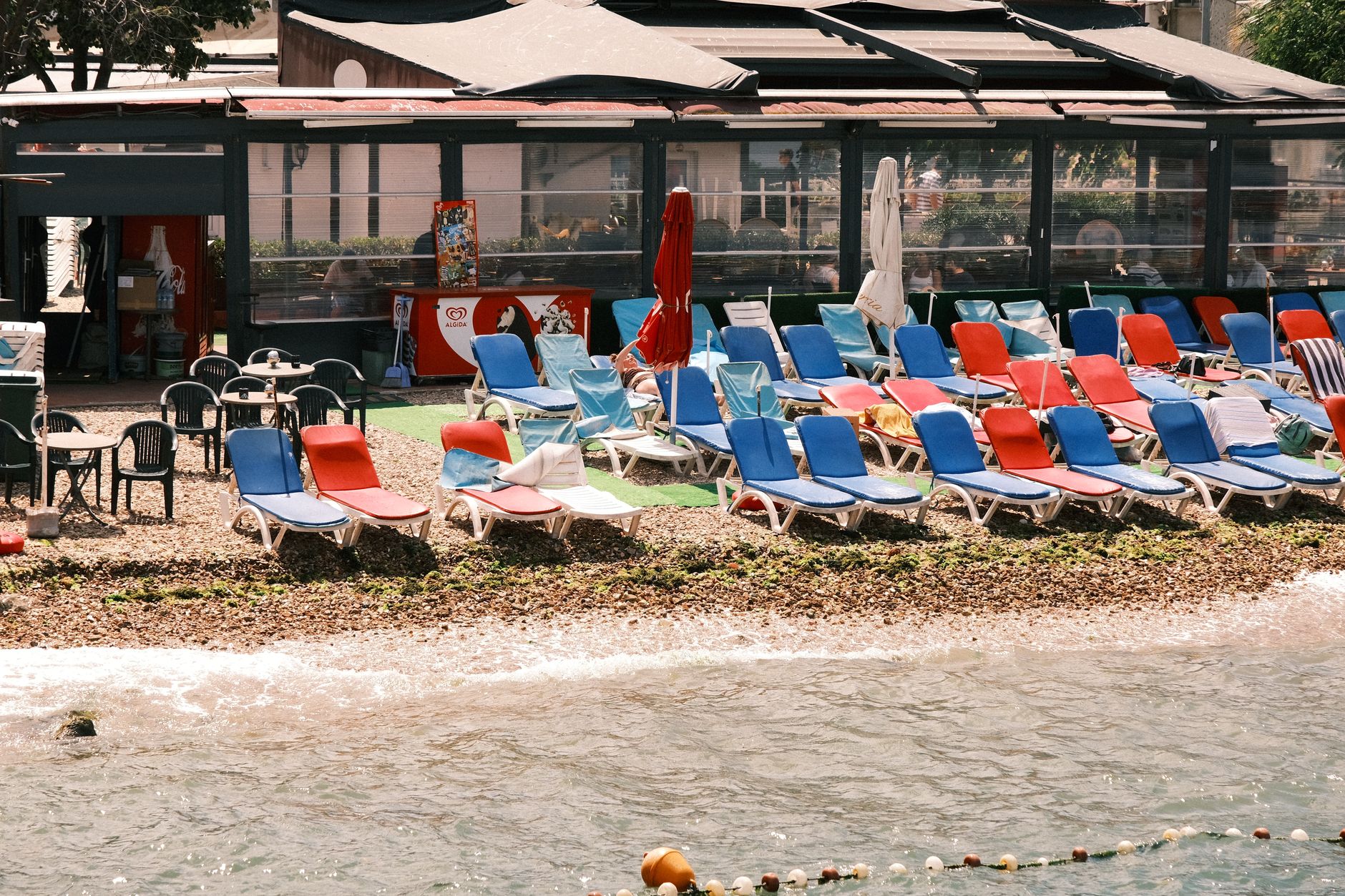 A vibrant seaside setting with colorful beach loungers in front of a café, ideal for summertime relaxation. — Trójmiasto