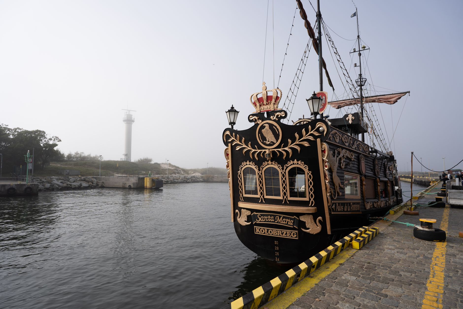 A decorative tall ship resembling Santa Maria docked at Kolobrzeg port with a lighthouse in view. — Trójmiasto