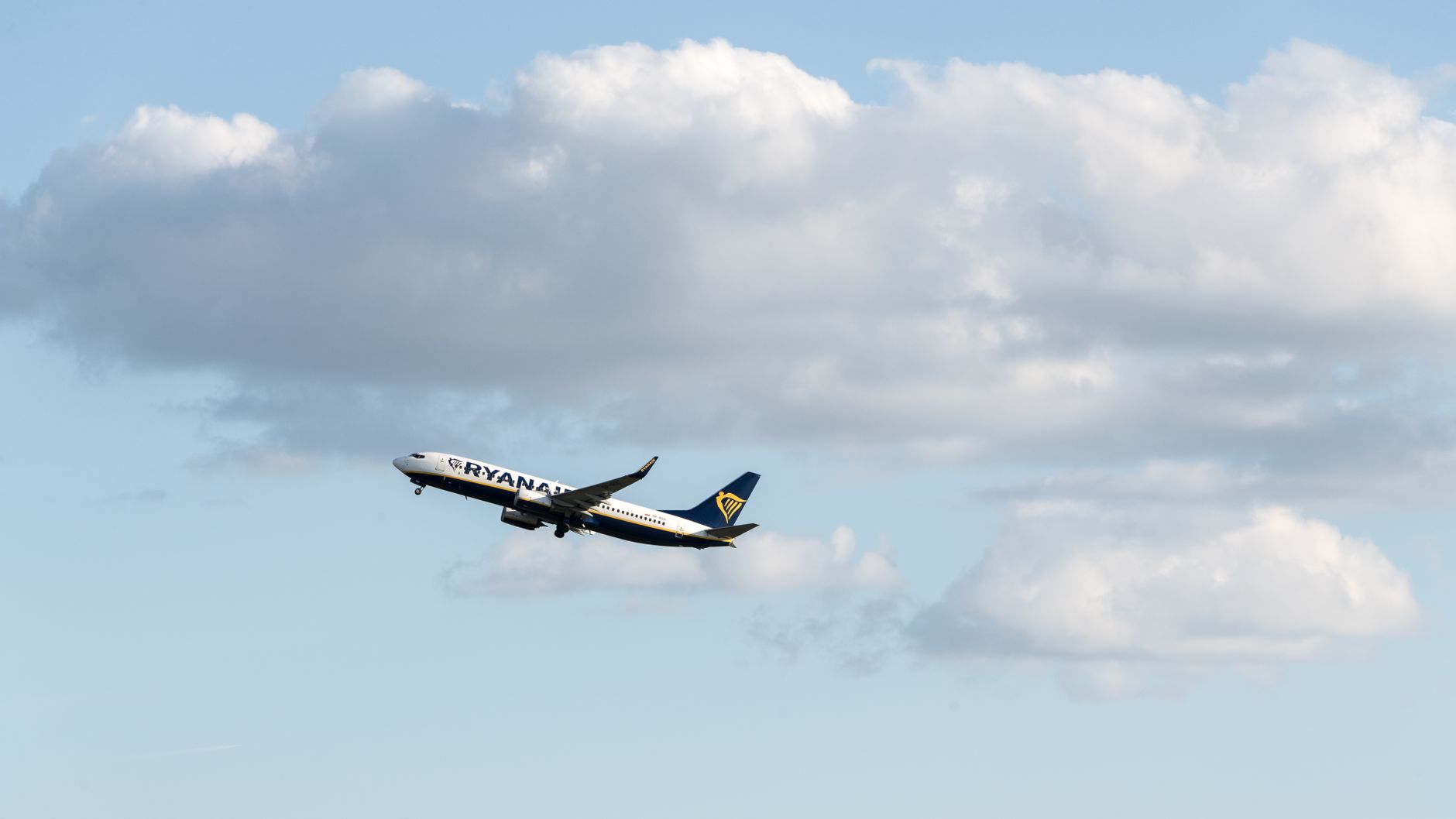 Ryanair airplane taking off into a clear blue sky with fluffy clouds in the backdrop. — Trójmiasto