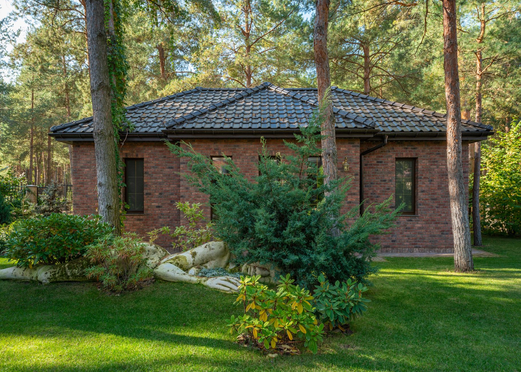 A modern brick house surrounded by a lush forest and lawn, featuring serene outdoor landscaping. — Trójmiasto