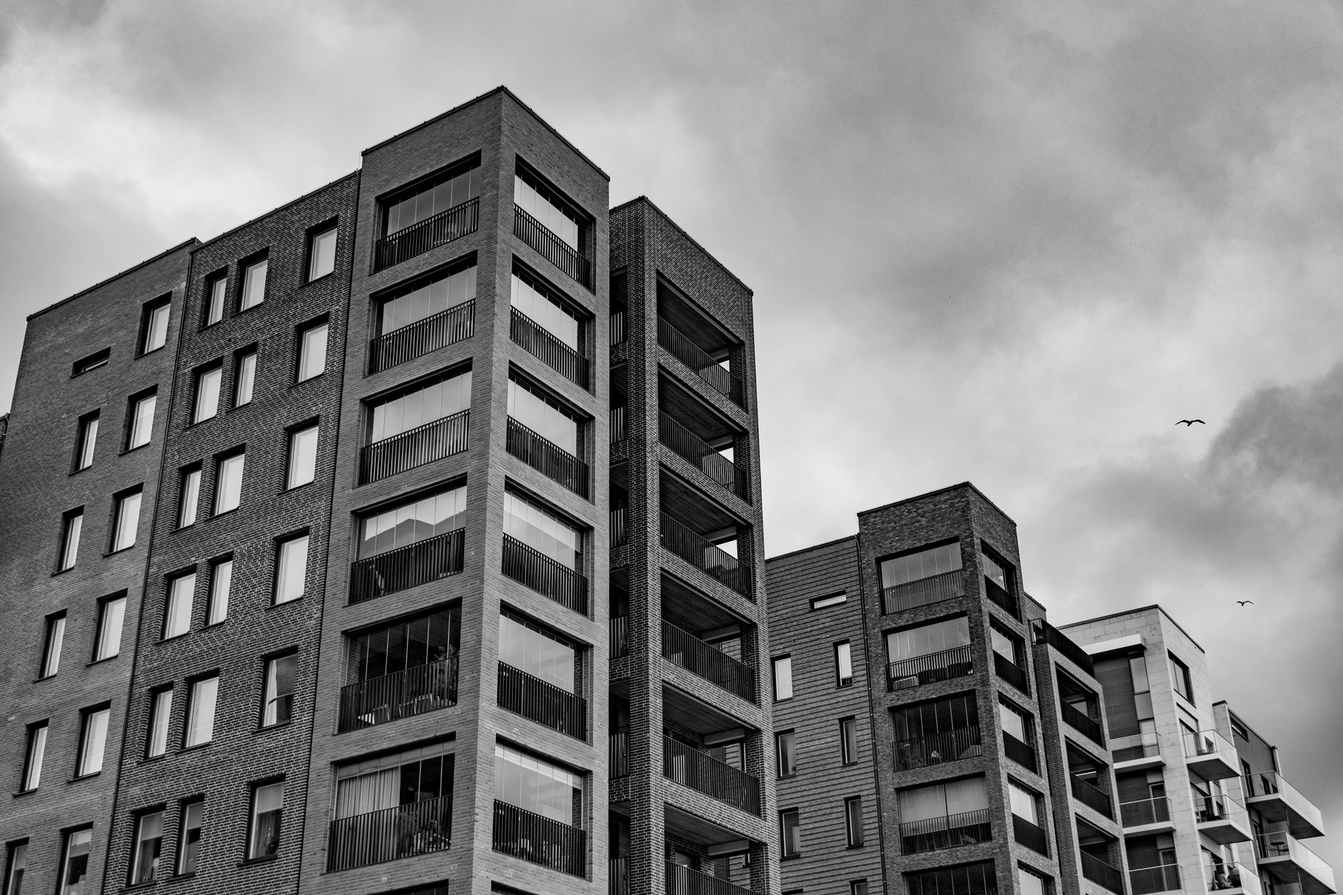 Black and white image of modern urban apartment buildings against a cloudy sky. — Trójmiasto