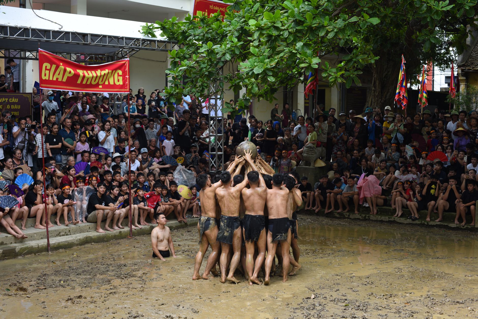 Participants engage in a traditional Vietnamese mud festival, cheered by a large crowd. — Trójmiasto