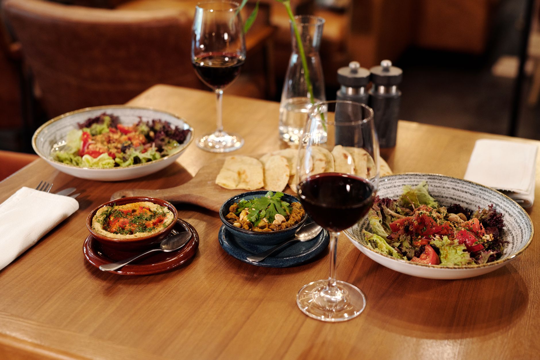 A beautifully arranged table featuring plates of Mediterranean food and glasses of red wine, set in a cozy restaurant atmosphere. — Trójmiasto