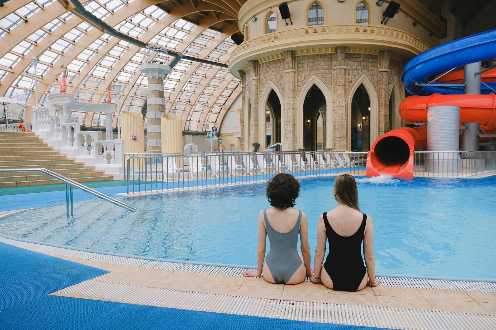 Two women in swimsuits sitting by an indoor pool with water slides. — Trójmiasto