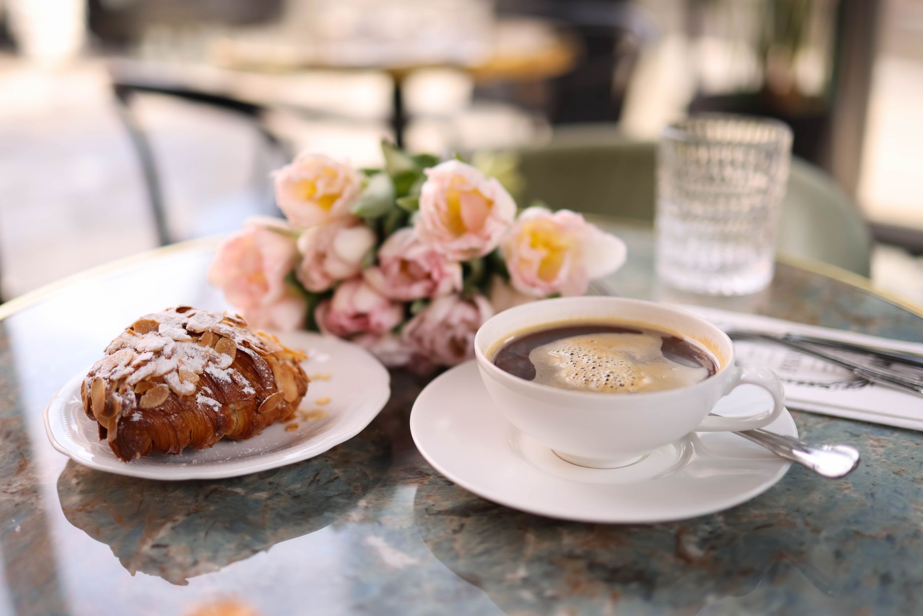 A stylish cafe table setup featuring a fresh croissant and a cup of coffee alongside a bouquet of flowers. — Trójmiasto