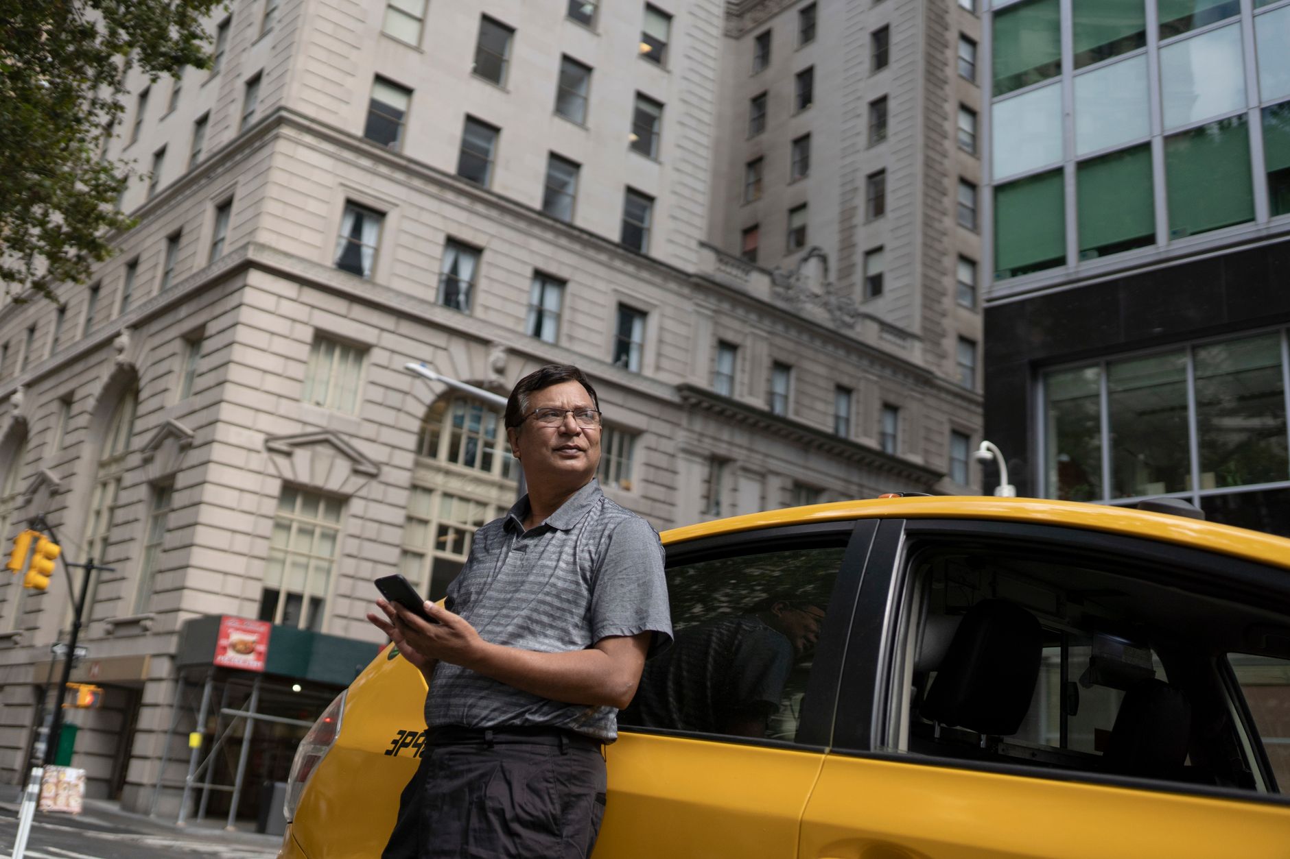 Low angle of serious ethnic male scrolling mobile phone while leaning on yellow car in downtown — Trójmiasto