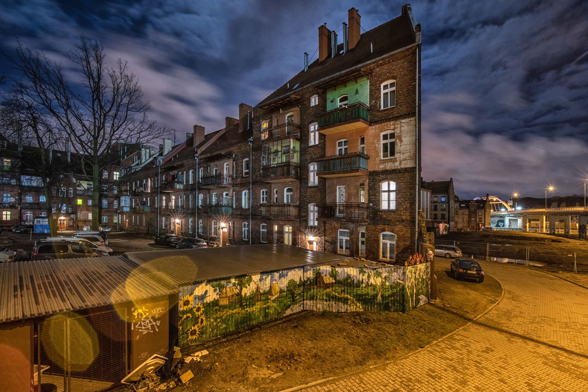 Facade of old houses located on city street near cars and road under dark cloudy sky in evening — Trójmiasto